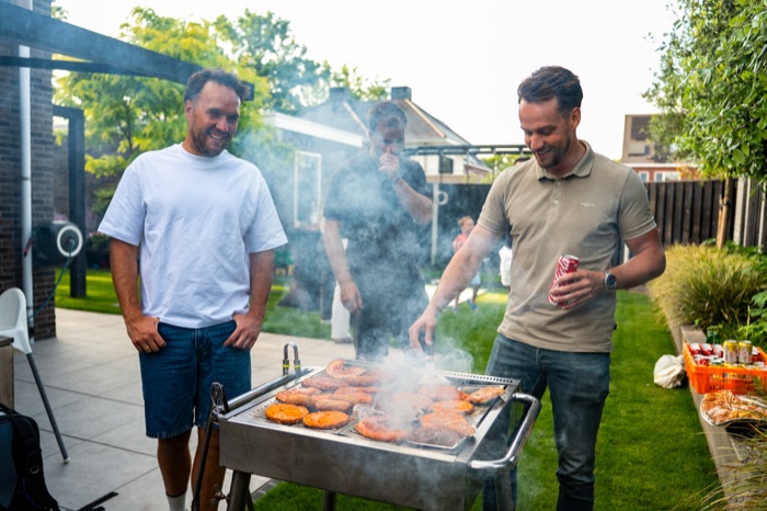 Vrienden lachend aan de barbecue in de tuin